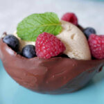 A chocolate bowl filled with fresh berries and ice cream and topped with a mint leaf.