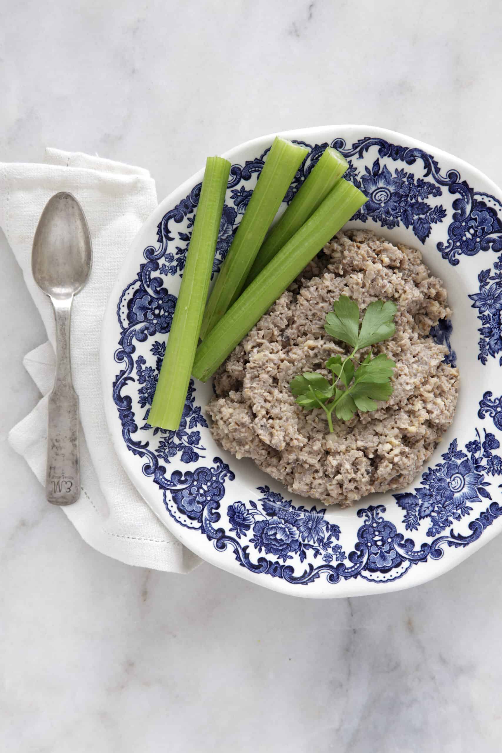 A blue and white bowl of vegan chopped liver accented by herbs and sticks of celery.