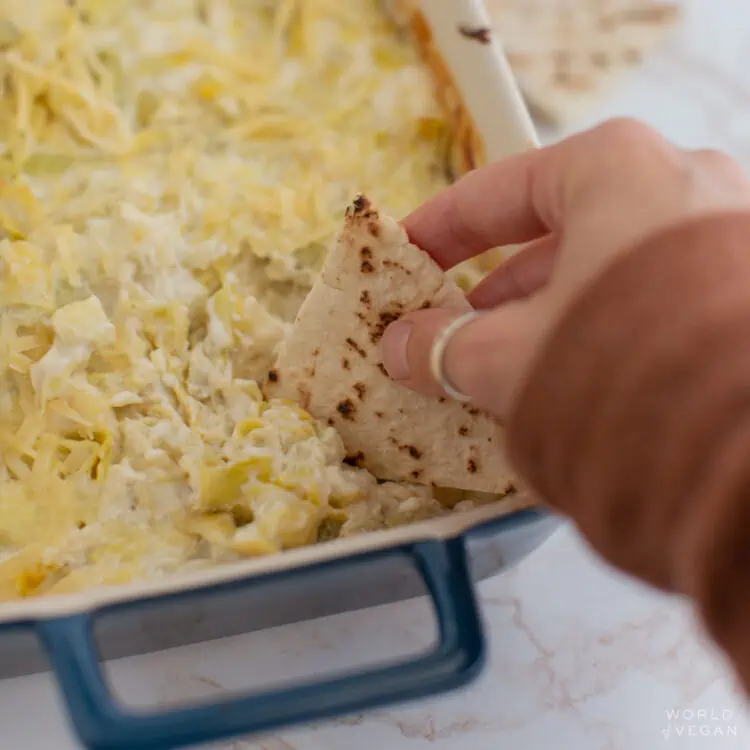 creamy vegan artichoke dip being scooped up with a piece of pita bread