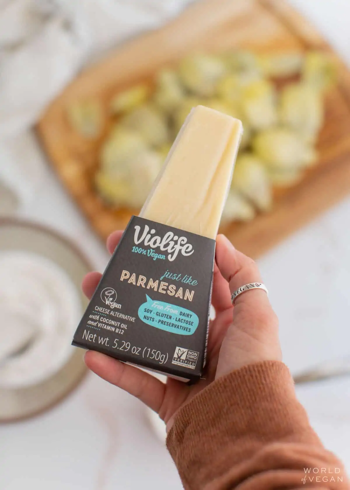 A hand holding a block of Violife brand vegan parmesan cheese.
