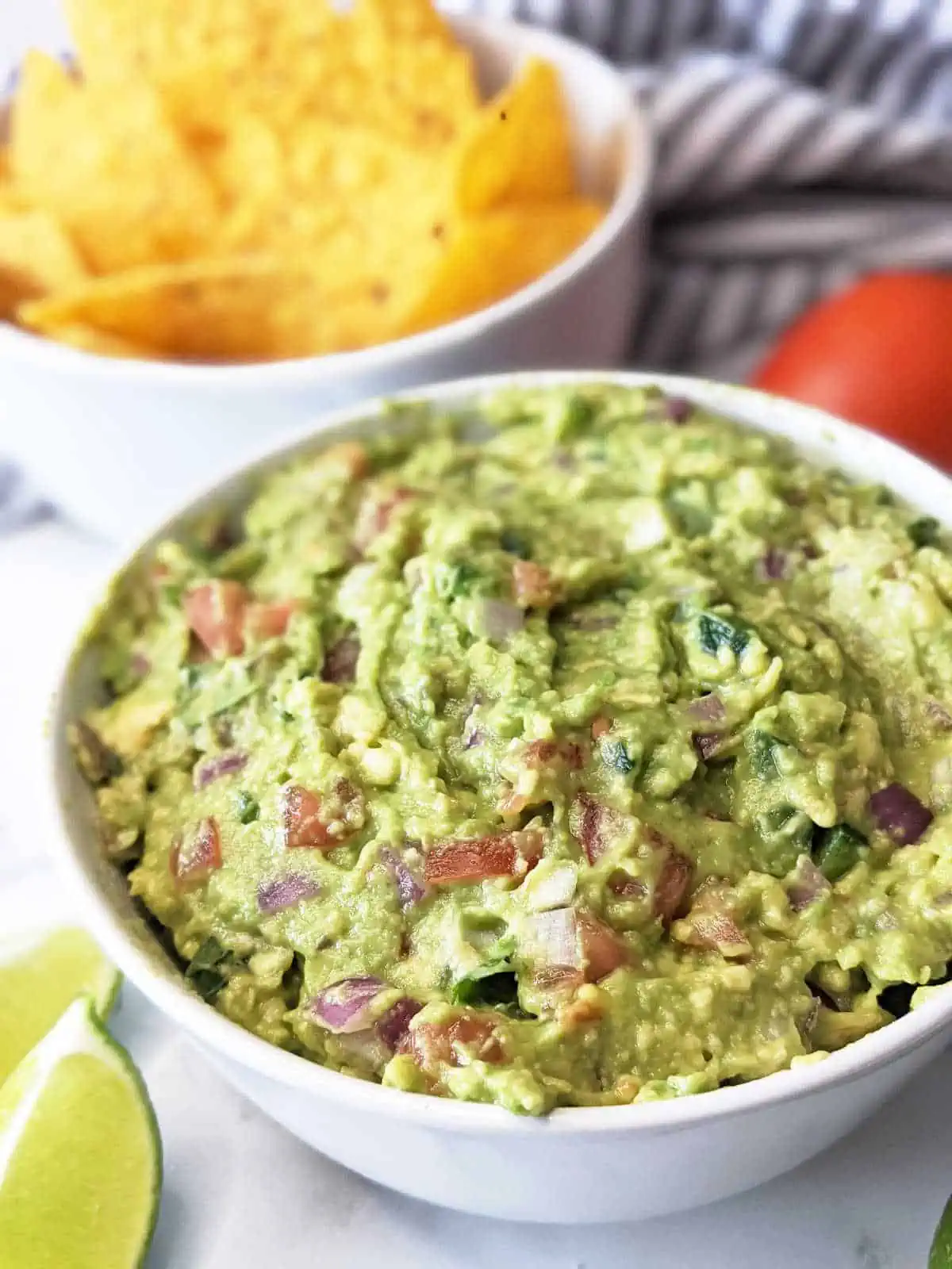 Vegan guacamole in a bowl next to a bowl of tortilla chips.