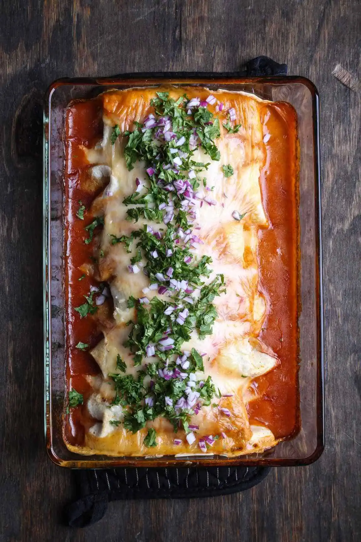 Sweet potato kidney bean burritos in a casserole dish smothered with sauce and vegan cheese.