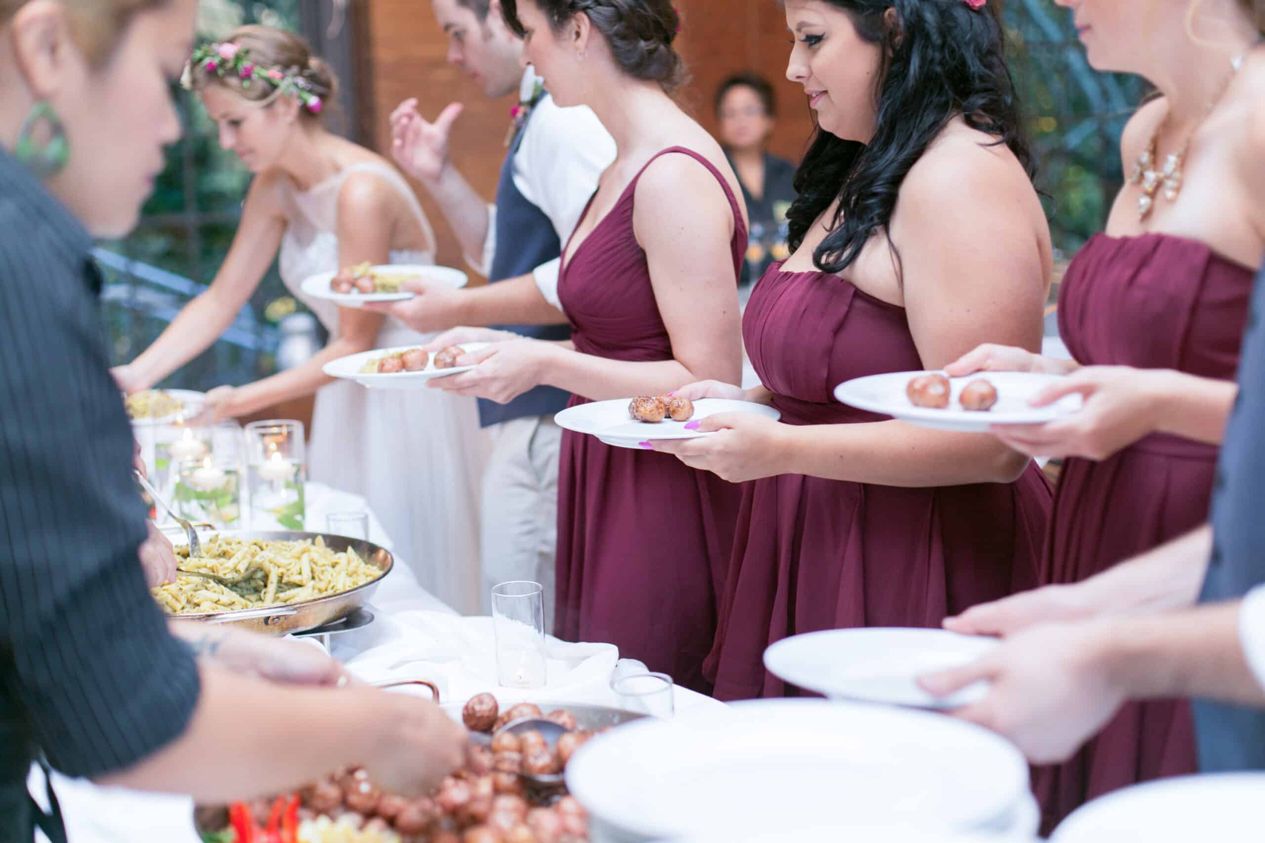 Bridesmaids in plum dresses lining up at the vegan wedding buffet.