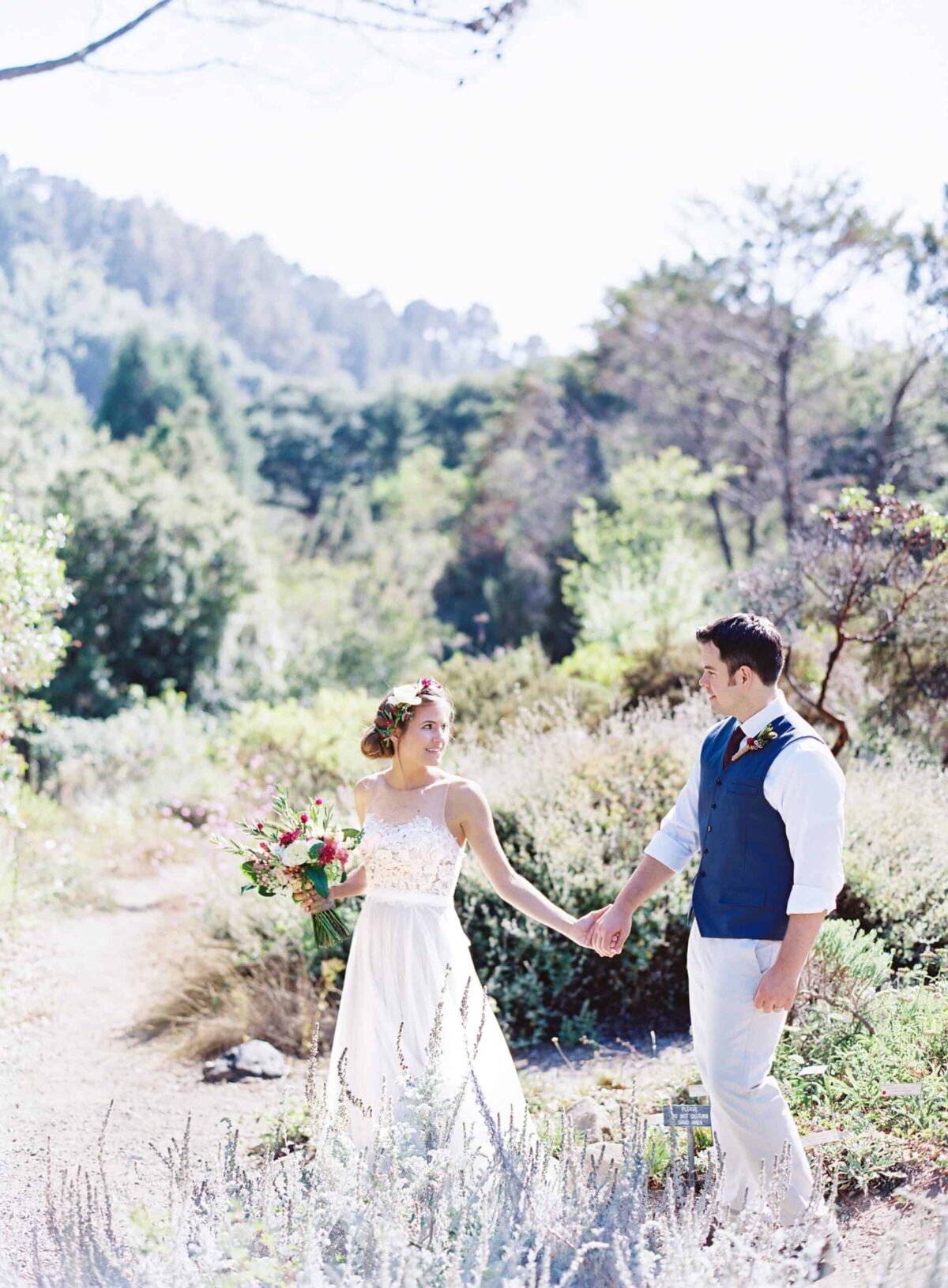 Bride and groom holding hands on a nature trail after their vegan wedding ceremony.