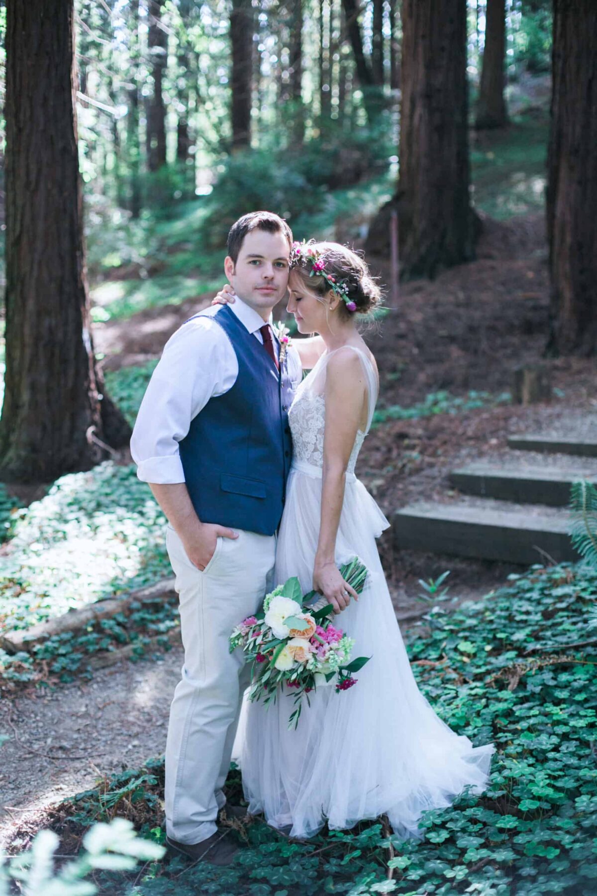 Bride and groom standing on stone steps surrounded by redwood trees.