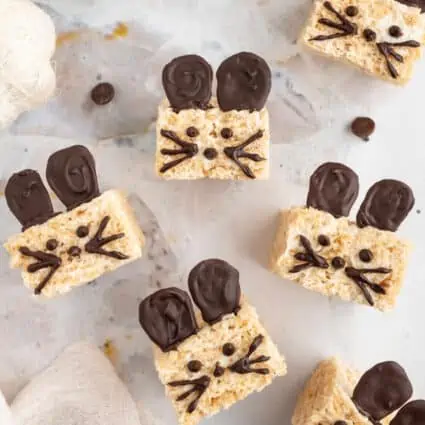 Rice krispie treats on a light background with mice faces drawn on with chocolate and chocolate ears.