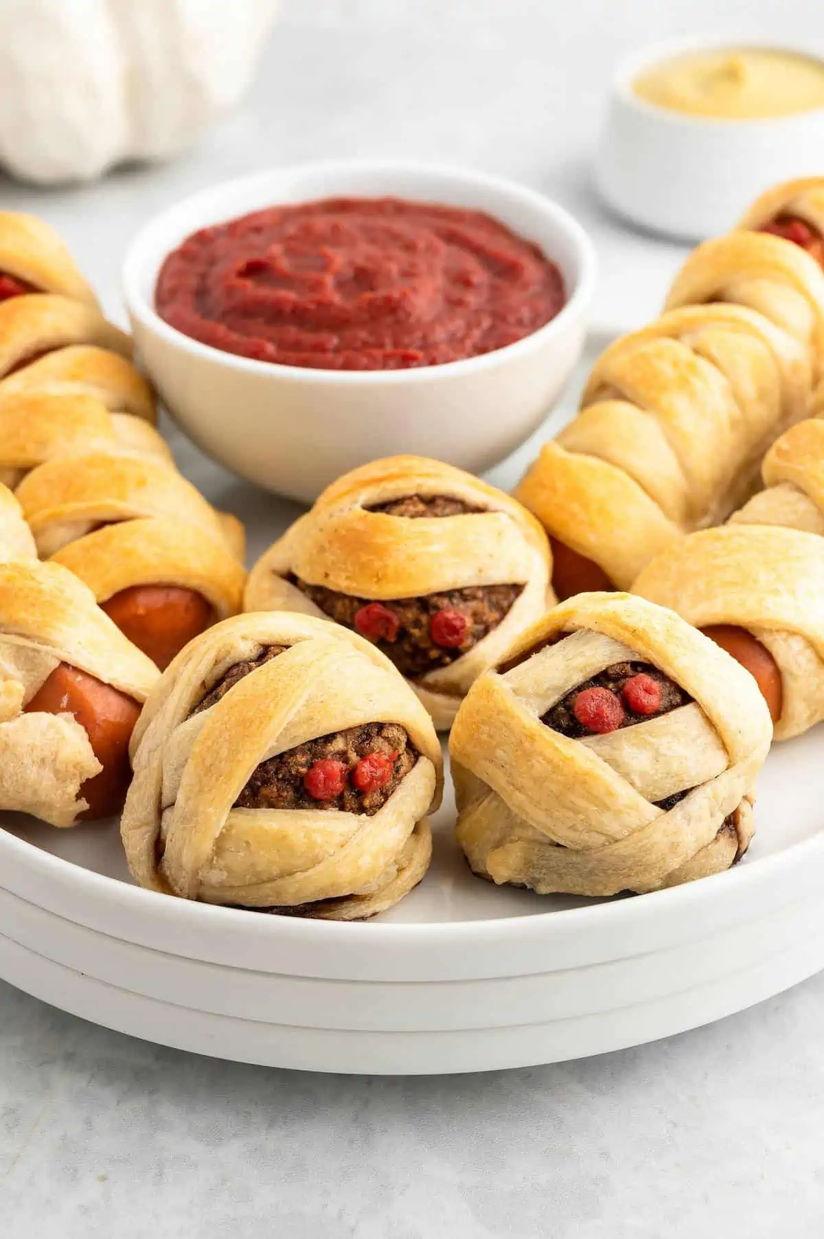 Mummy balls and mummy dogs on a plate serve with a bowl of ketchup.