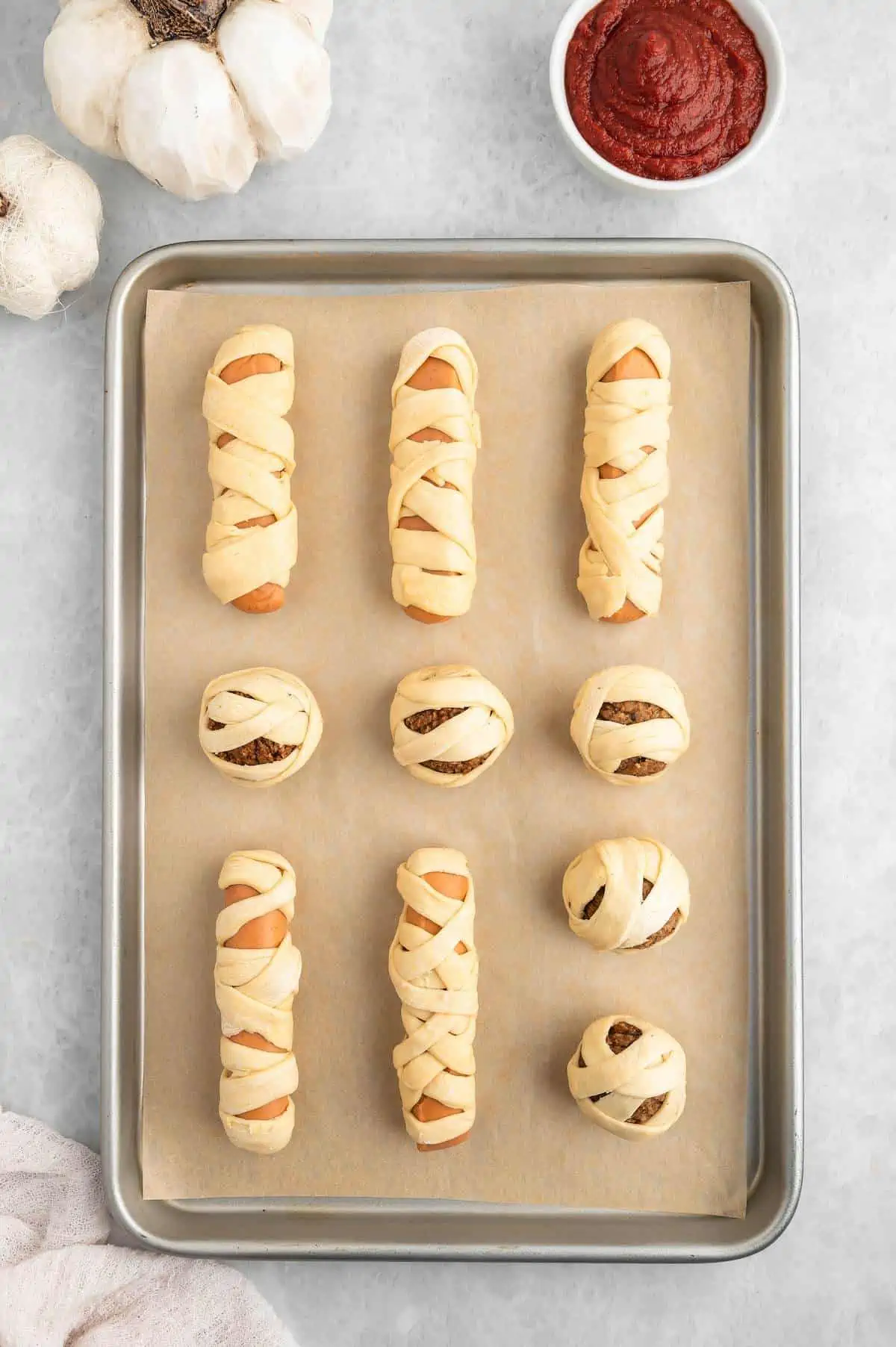 Wrapped and ready to bake mummy balls and dogs on a baking tray lined with parchment paper.