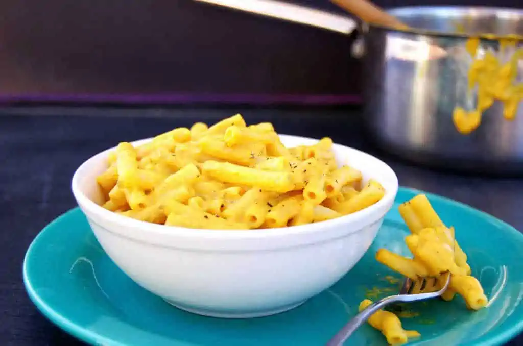 Bowl of dairy-free mac and cheese on a plate with a fork holding some noodles.