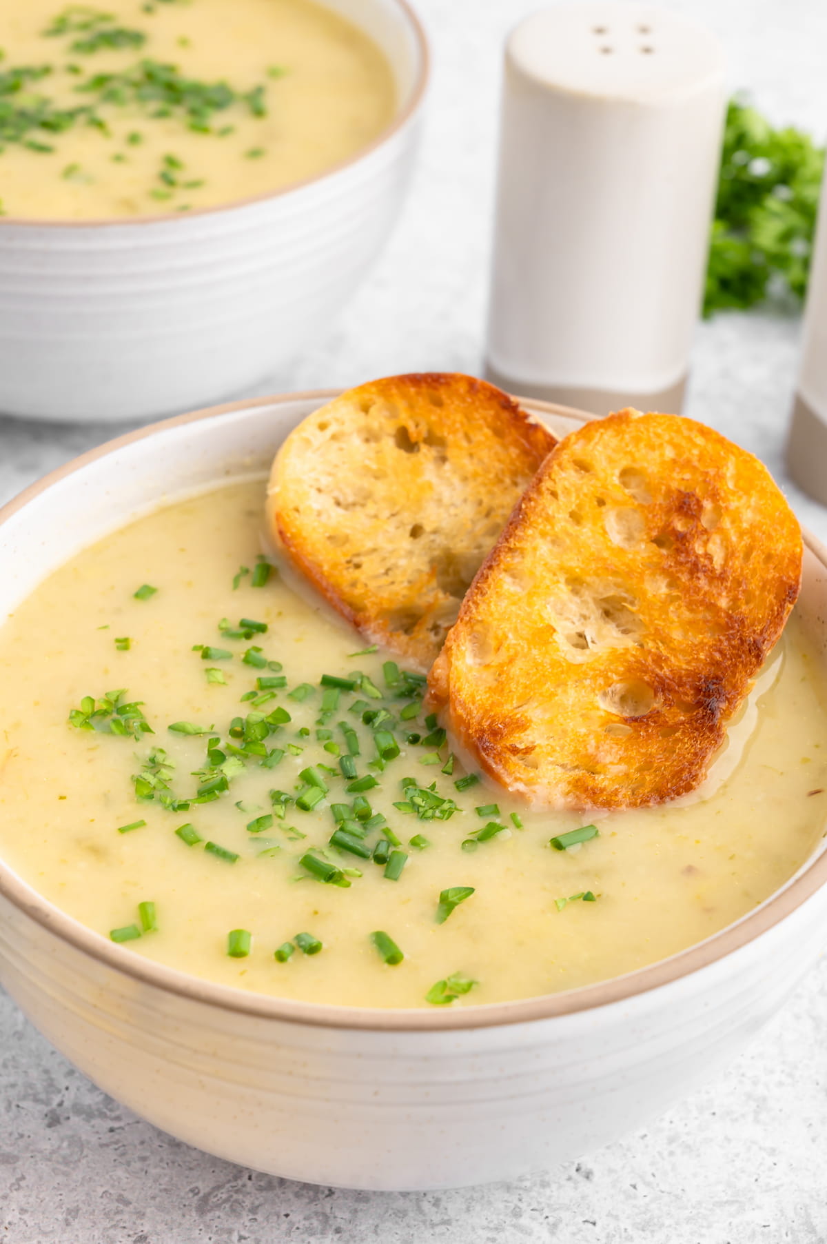 Vegan potato leek soup in a bowl with chopped chives and toasted bread slices.