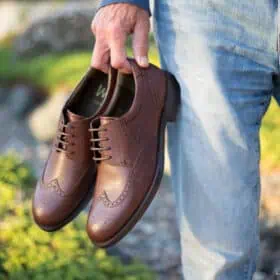 Man holding a pair of brown Will vegan shoes.