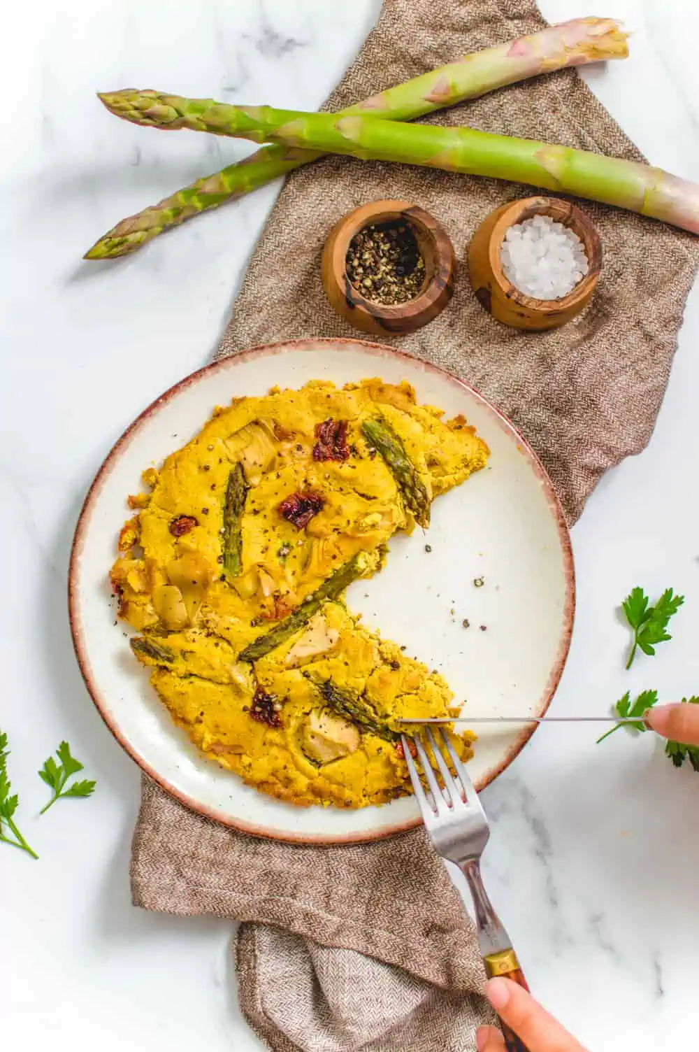 Vegan frittata with asparagus, artichokes, and sun-dried tomatoes on a plate with a slice missing.