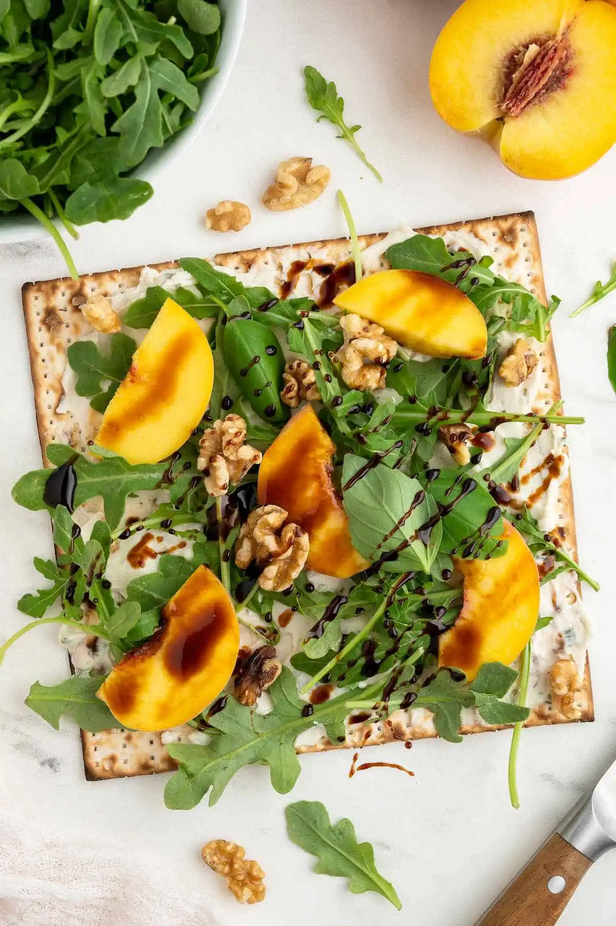 Matzah pizza topped with vegan cream cheese, arugula, basil, peach slices, walnuts and balsamic glaze.