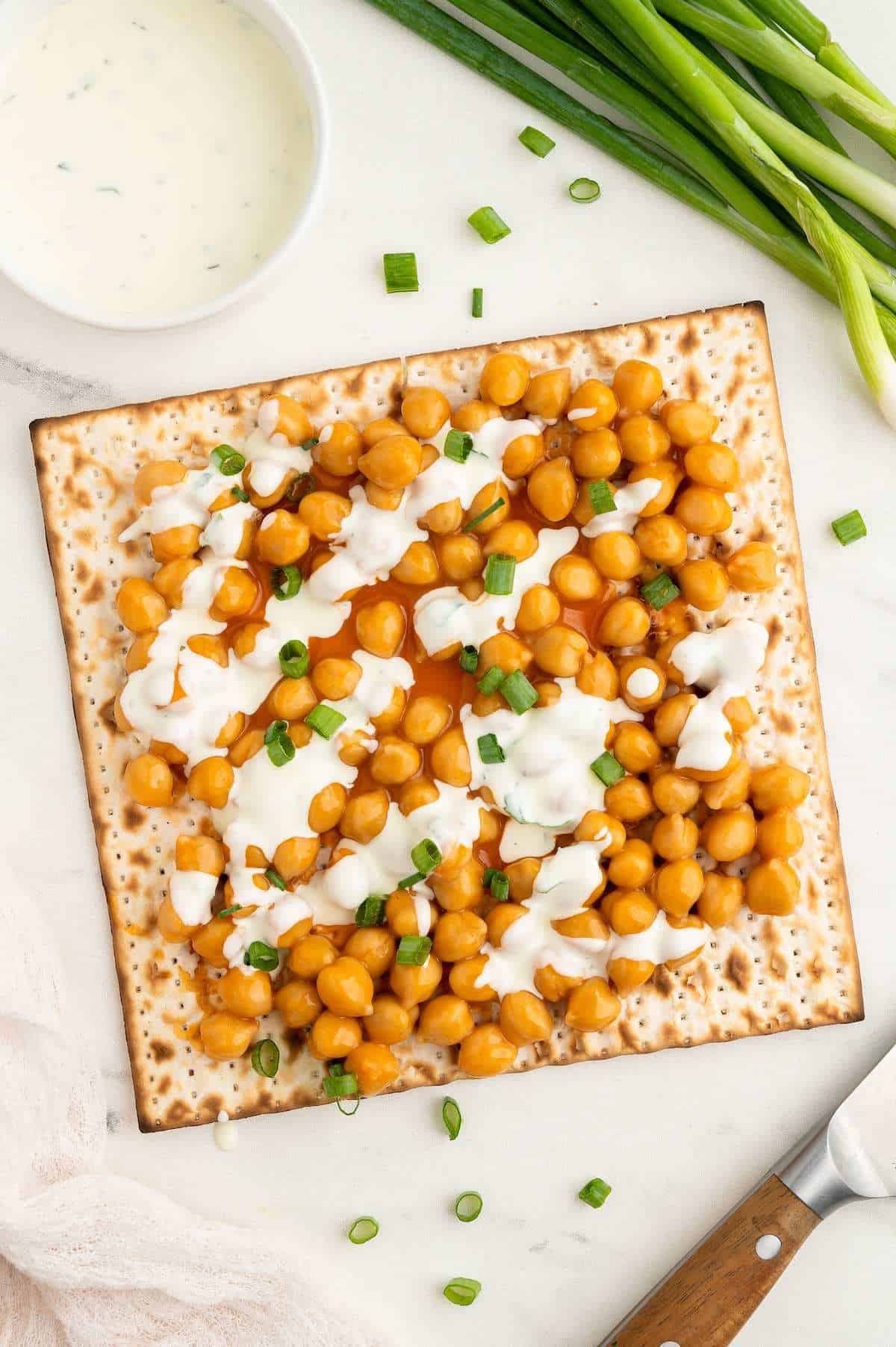 Matzah cracker topped with chickpeas tossed in buffalo sauce, vegan ranch (used recipe from buffalo cauliflower), and green onions.