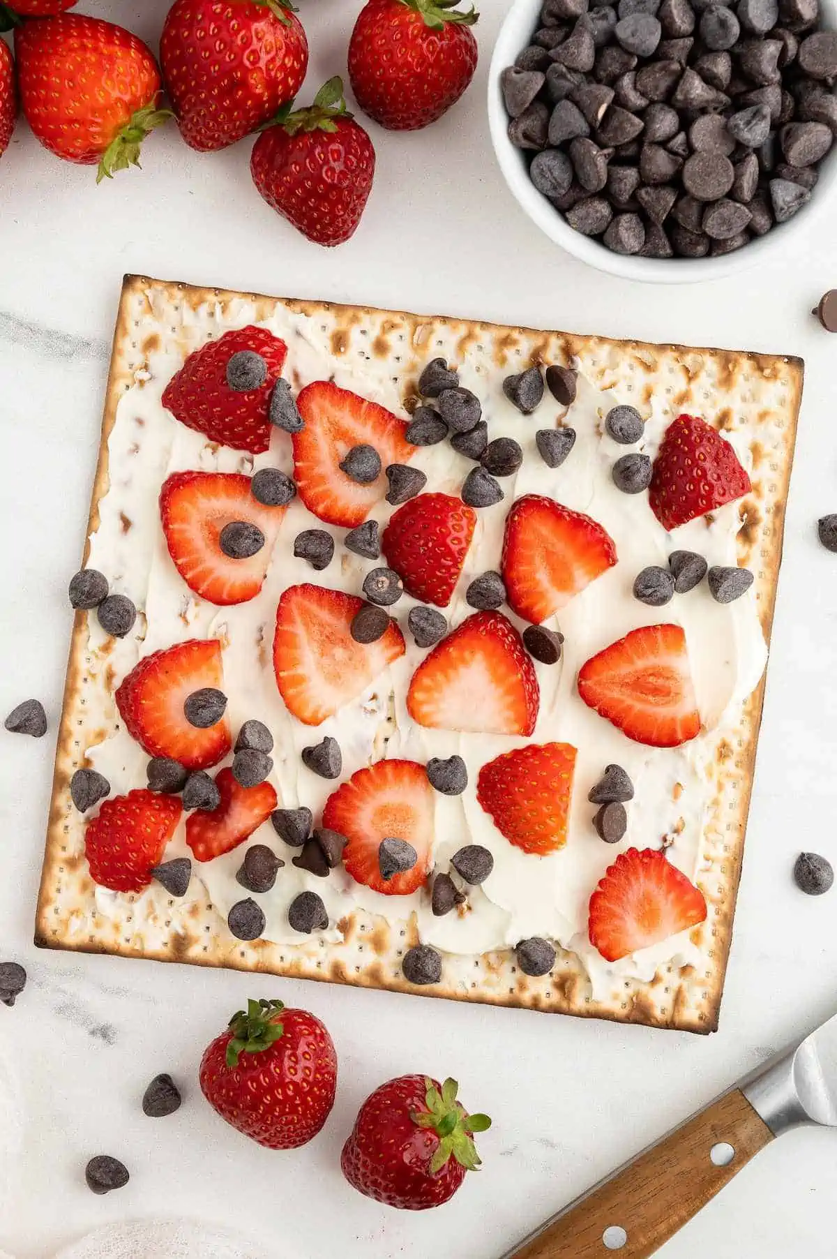 Matzah cracker topped with Plain vegan cream cheese, sliced strawberries, and dairy-free chocolate chips.