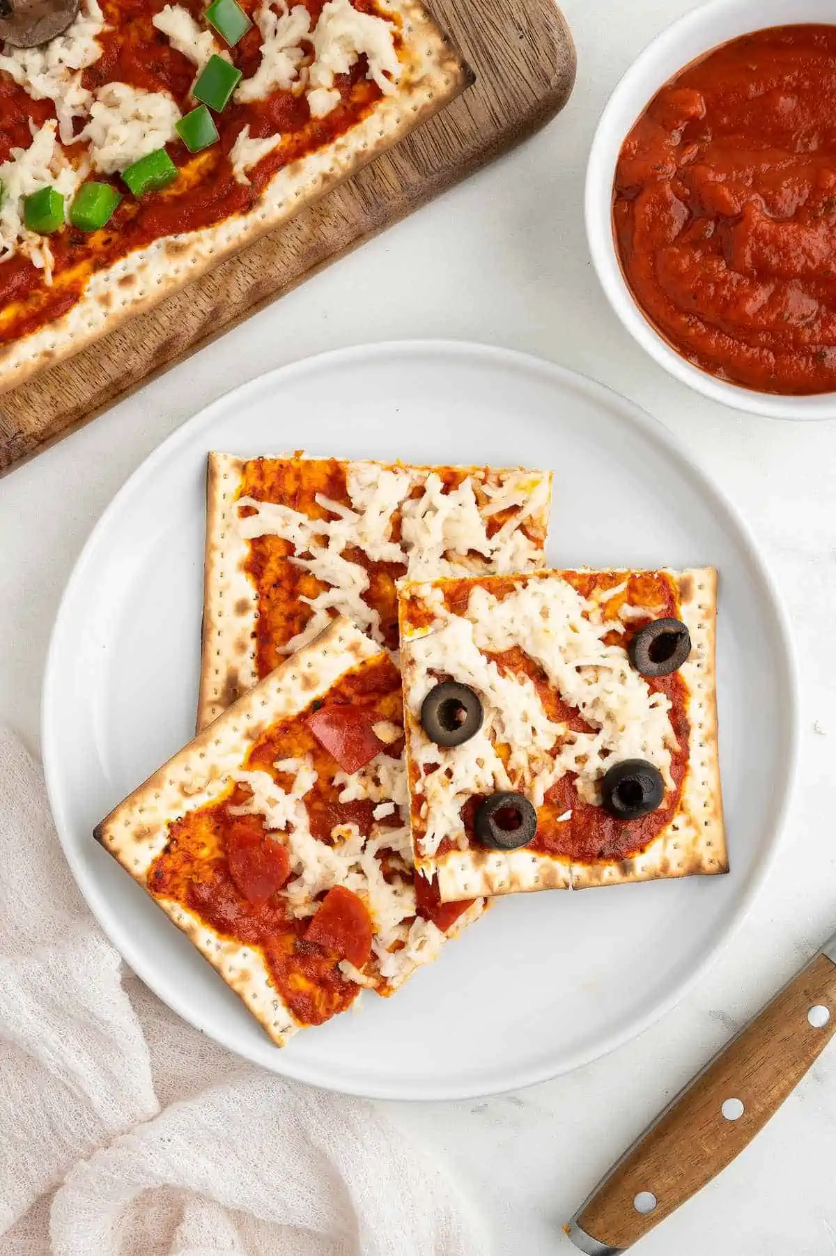 Three slices of matzah pizza topped with olives and vegan pepperoni on a plate.