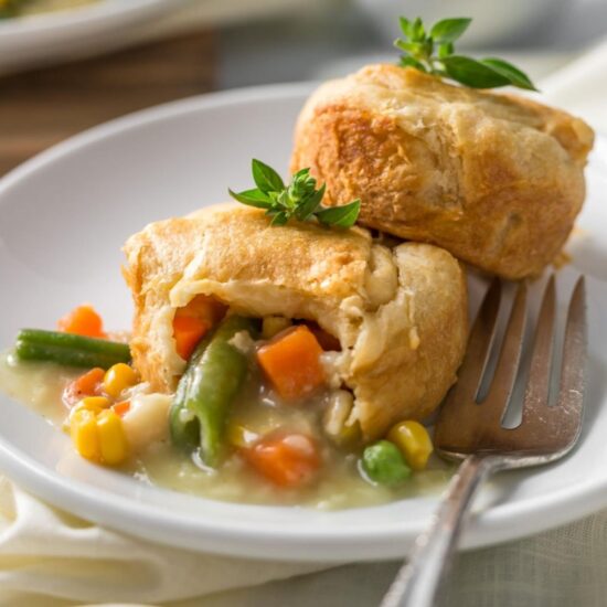 Two mini vegan pot pies on a plate with one sliced open to reveal the filling and veggies.