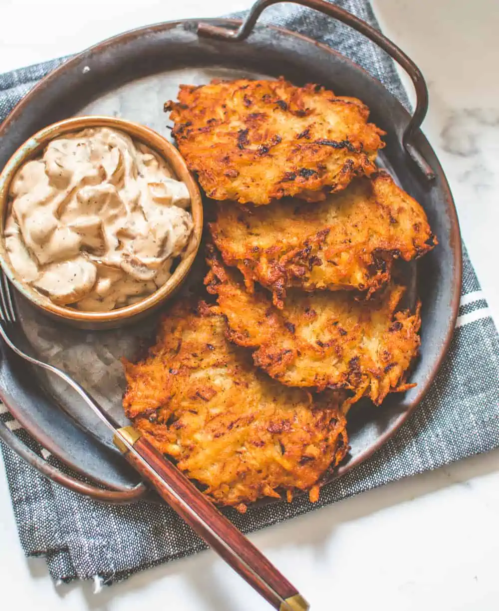 Four crispy vegan potato latkes served on a platter with caramelized onion dip.