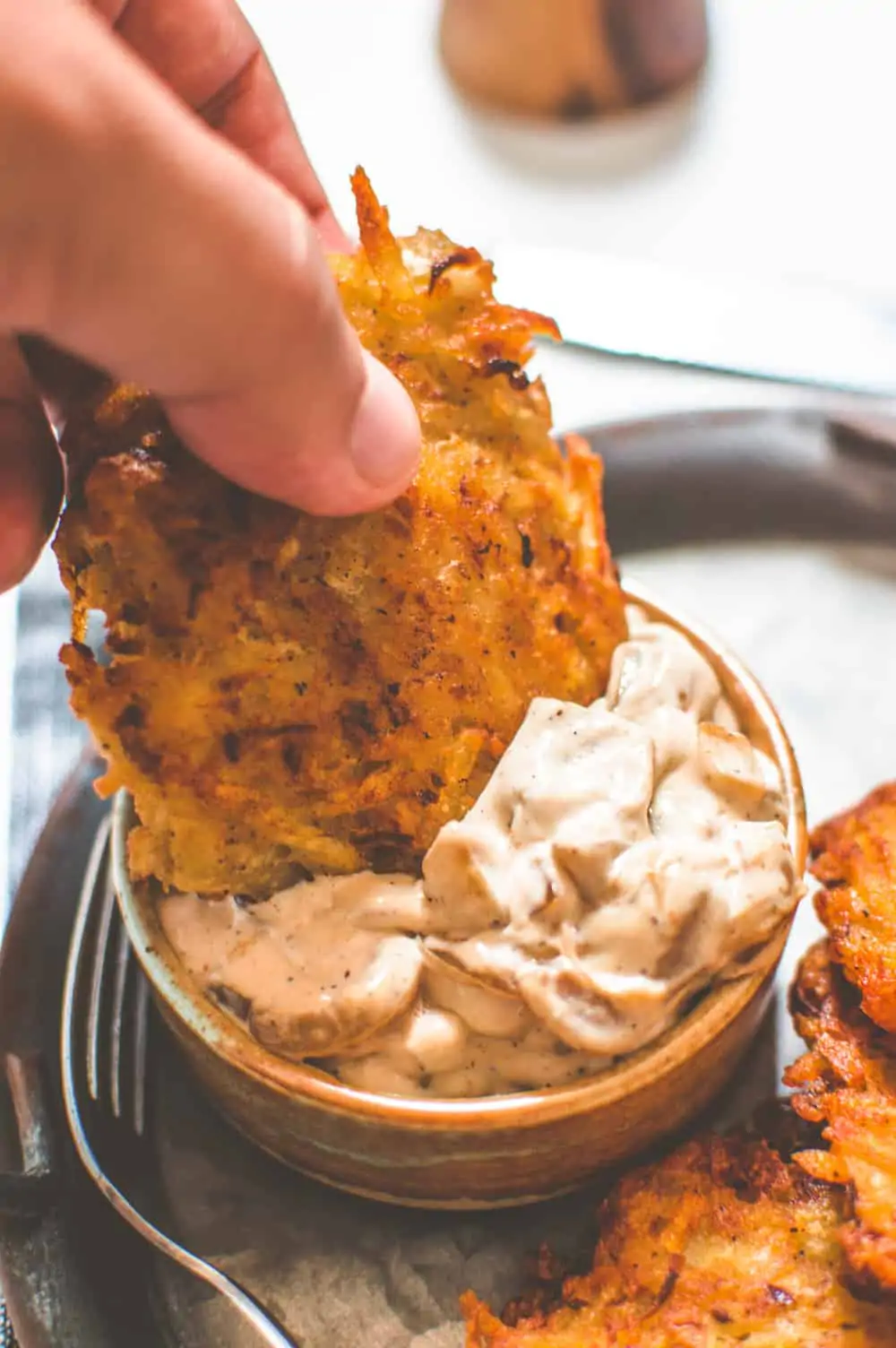 A hand dipping a vegan potato latke into caramelized onion dip.