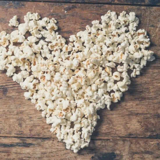A pile of popcorn shaped like a heart on a wooden background.