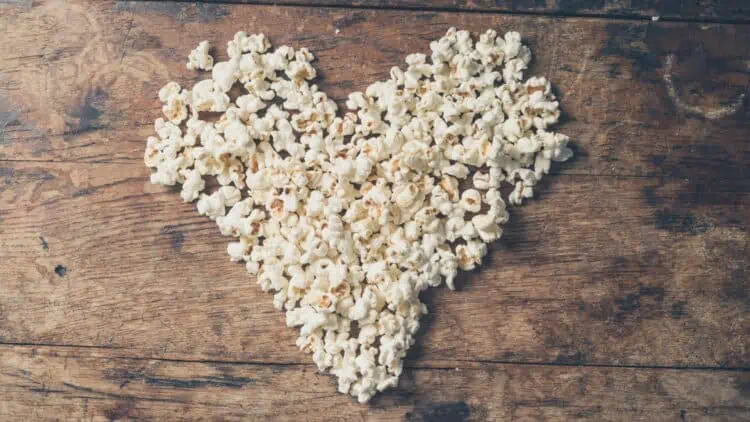 A pile of popcorn shaped like a heart on a wooden background.