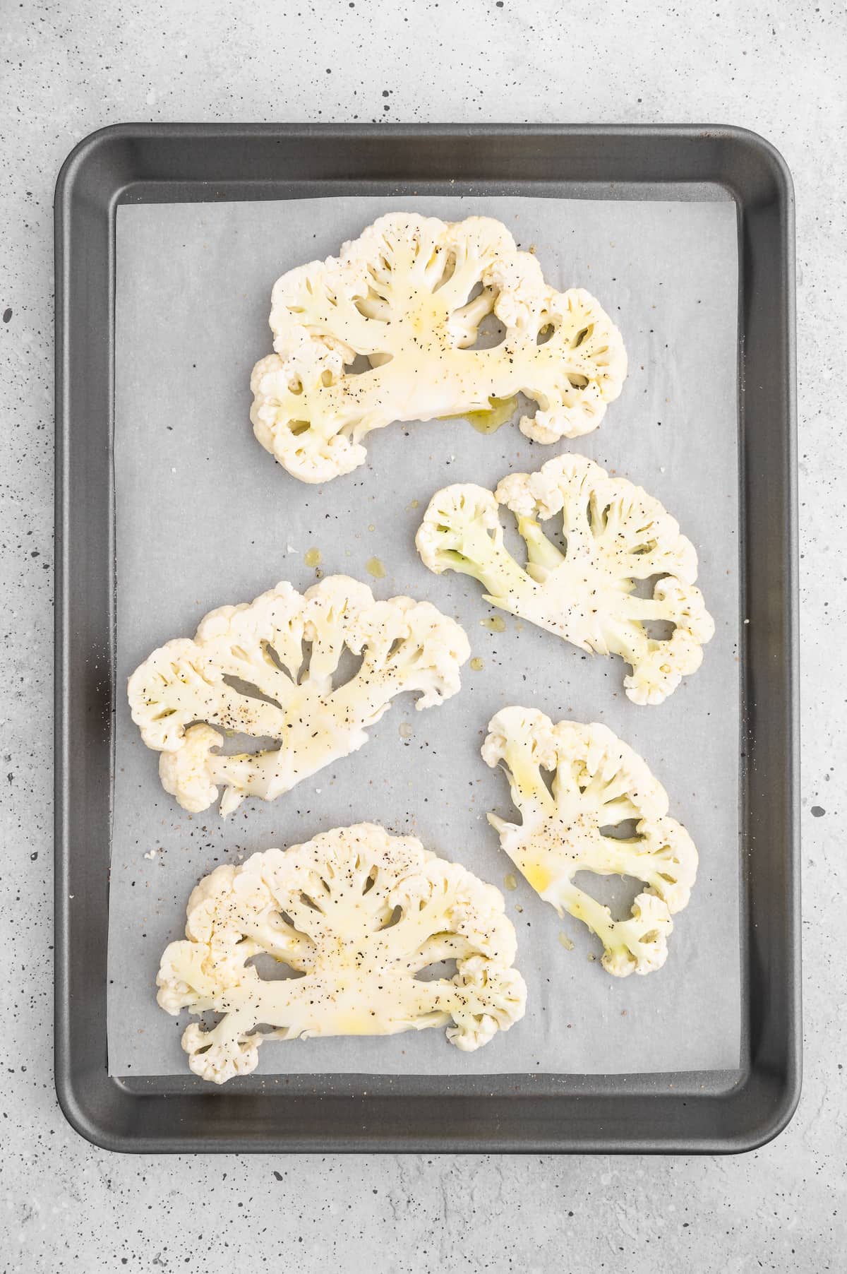 The cauliflower steaks on a baking tray after adding oil, salt, and pepper.