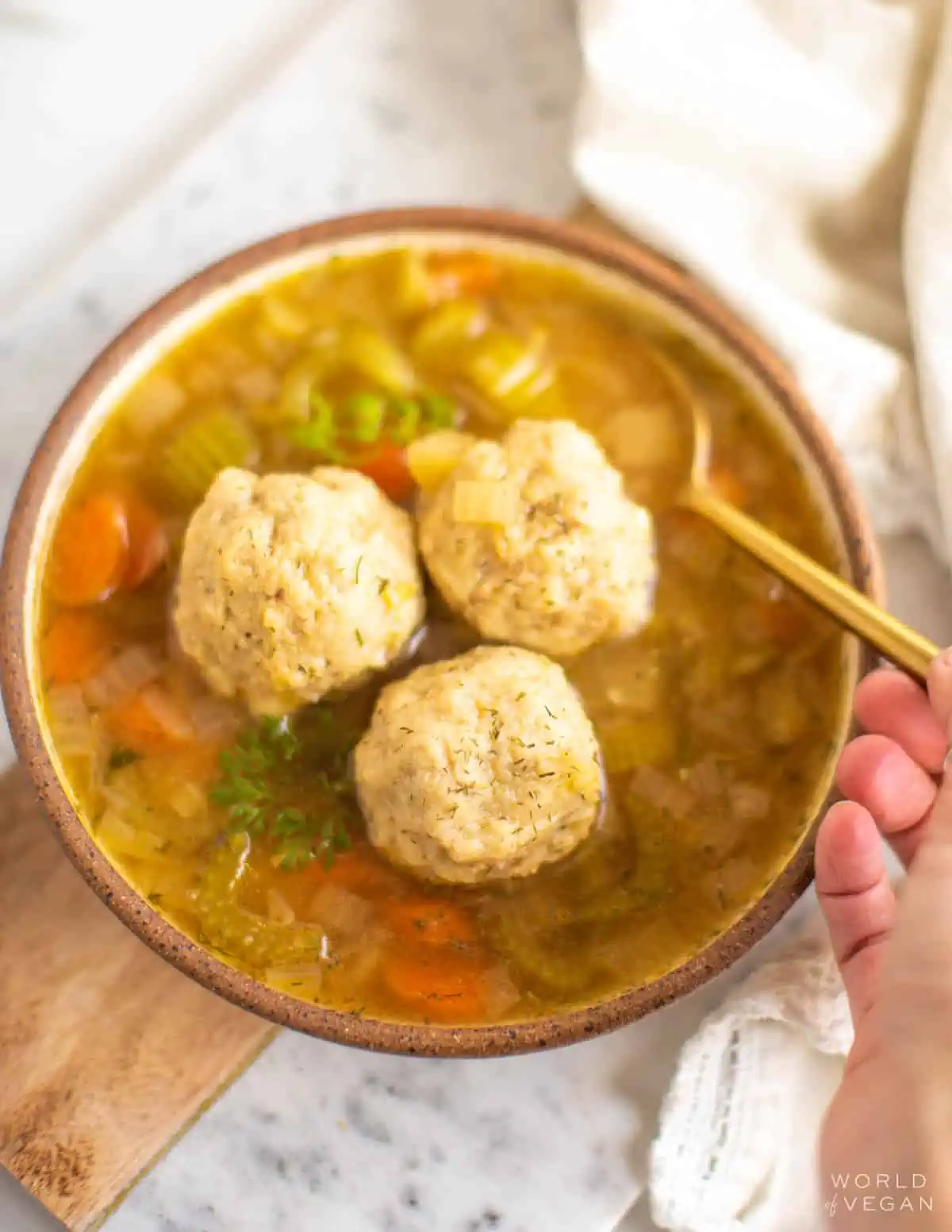 A hot bowl of vegan matzo ball soup with three matzo balls inside the vegetarian broth.