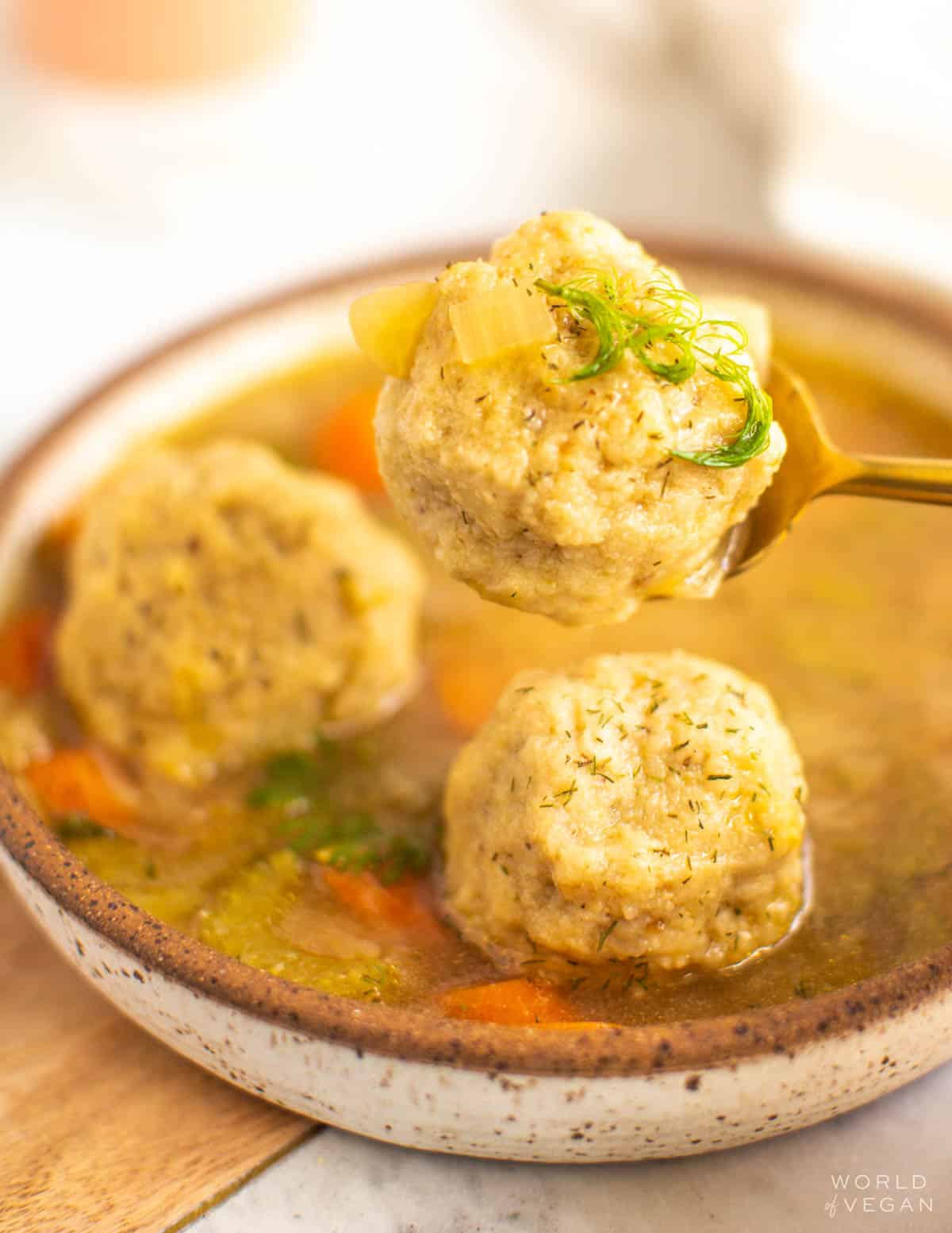 Spoon scooping up a vegan matzo ball from a bowl of soup up-close. 