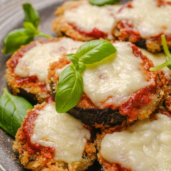 Slices of vegan eggplant parmesan on a plate, topped with fresh basil leaves.