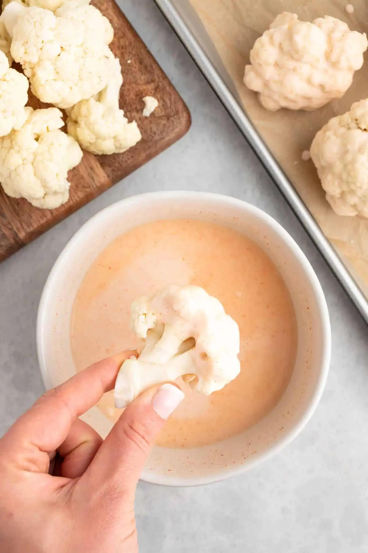 Hand dipping a cauliflower floret into the prepared buffalo sauce batter.