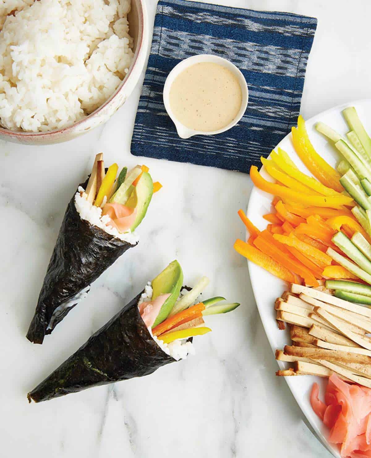 Hand rolls with baked tofu and veggies on a table with rice.