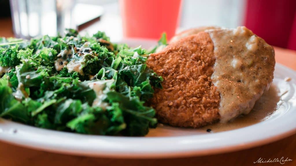 vegan fried chicken with gravy and sauteed kale on a white plate