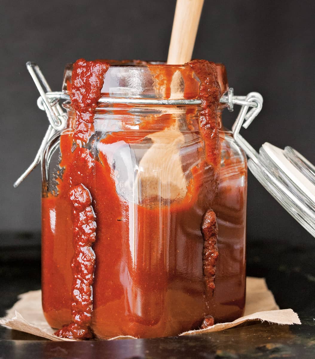 Glass jar filled with vegan barbecue sauce and some running down the sides.