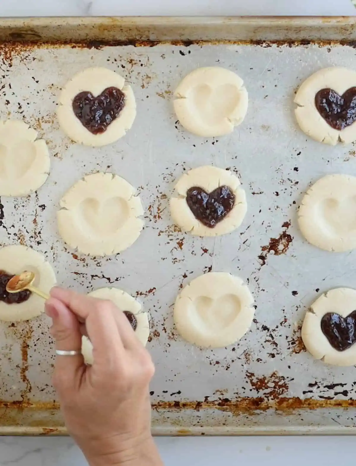 Hand spooning jam into the heart shaped dents of the prepared cookies.