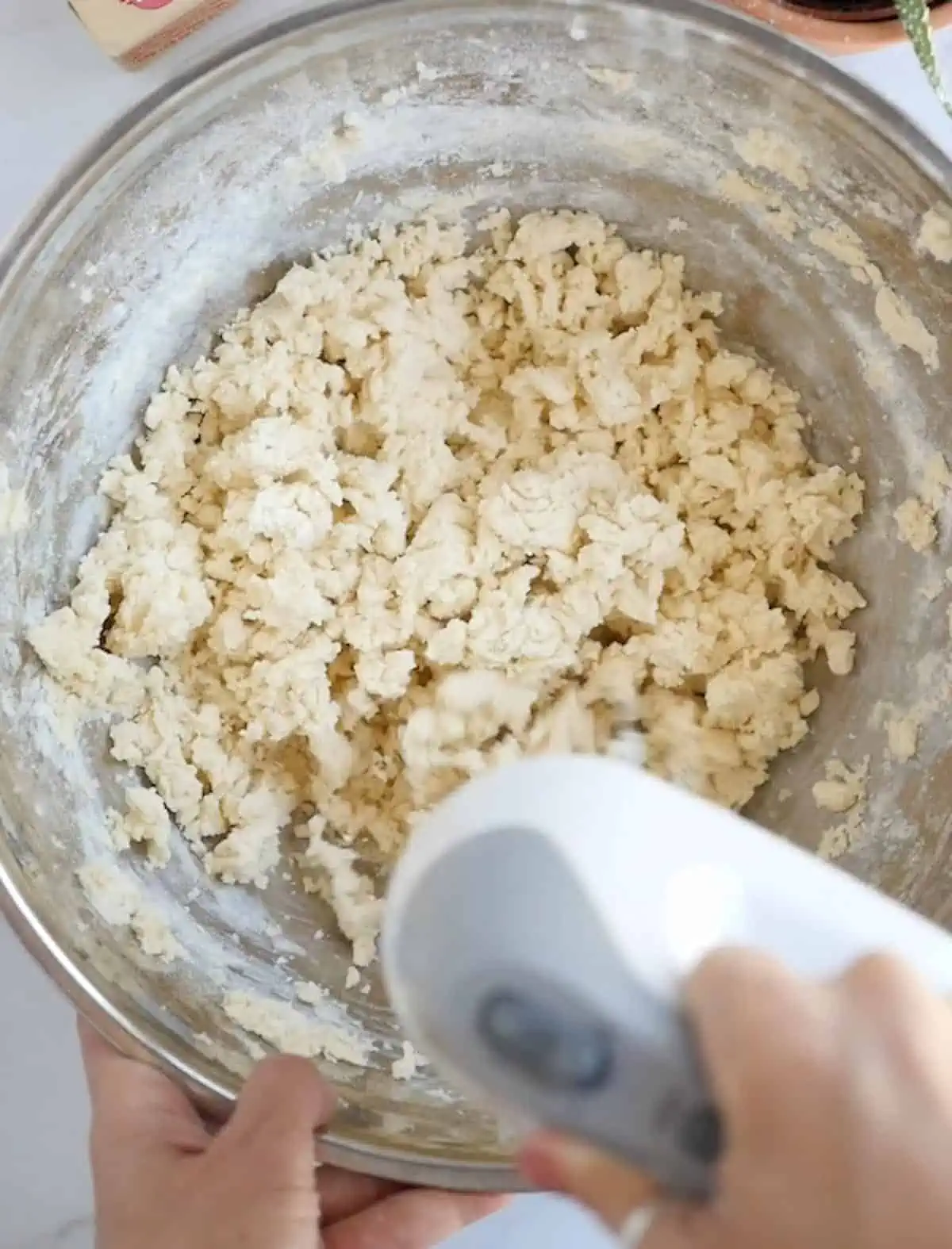 Crumbly vegan sugar cookie batter that is being mixed with an electric hand mixer.