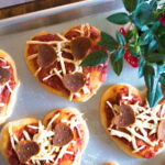 Mini heart shaped pizzas on a baking tray.