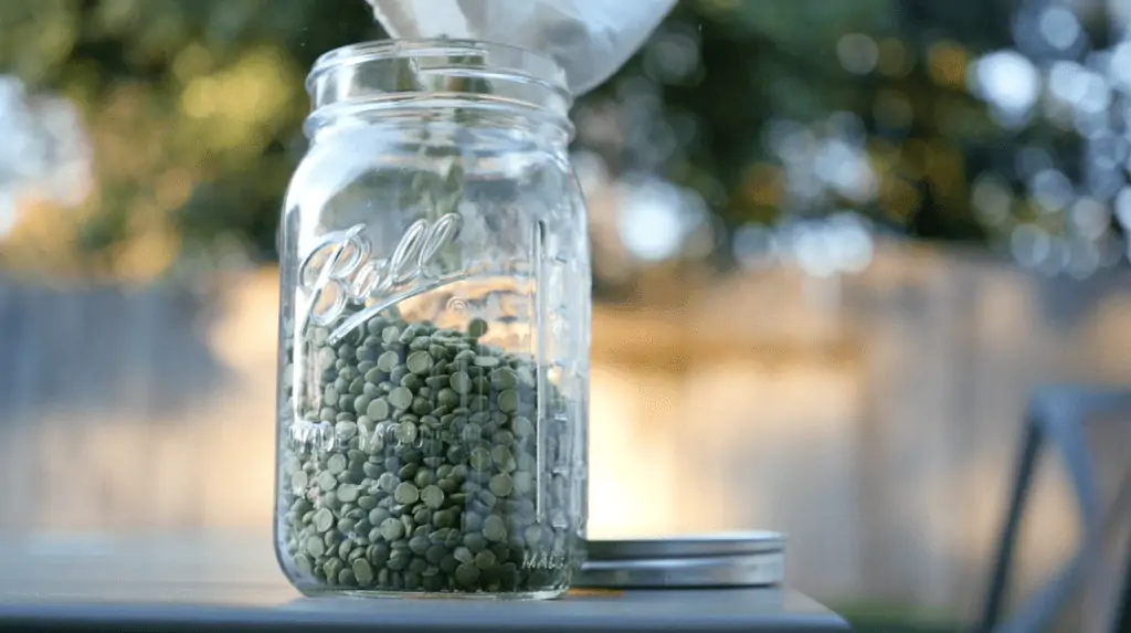 Green lentils being poured into a glass Ball Mason jar