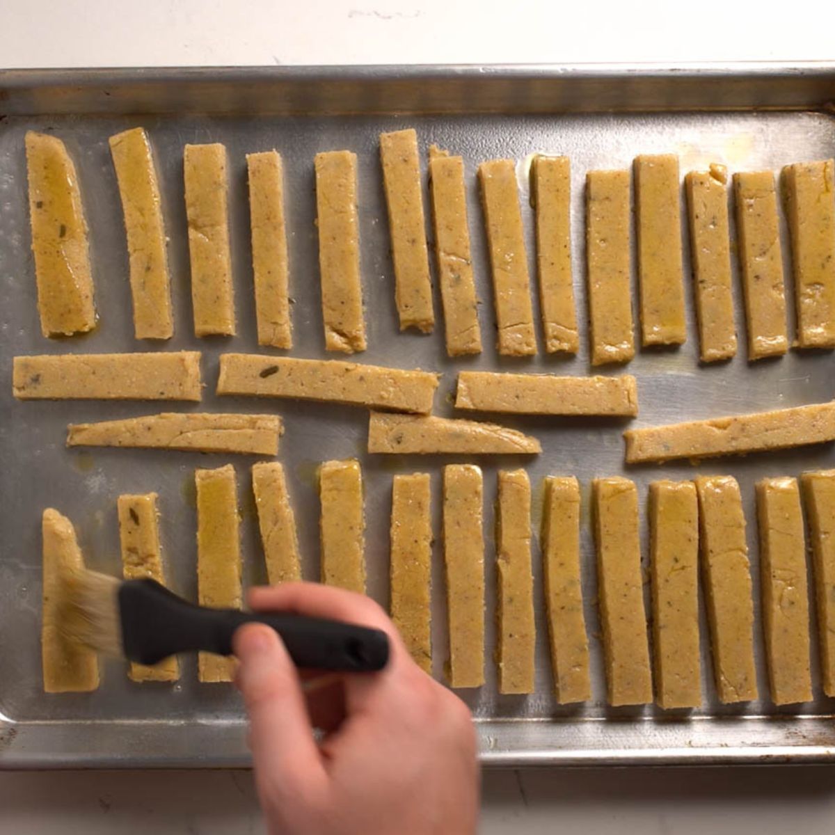 Polenta fries on a baking sheet being brushed with oil.