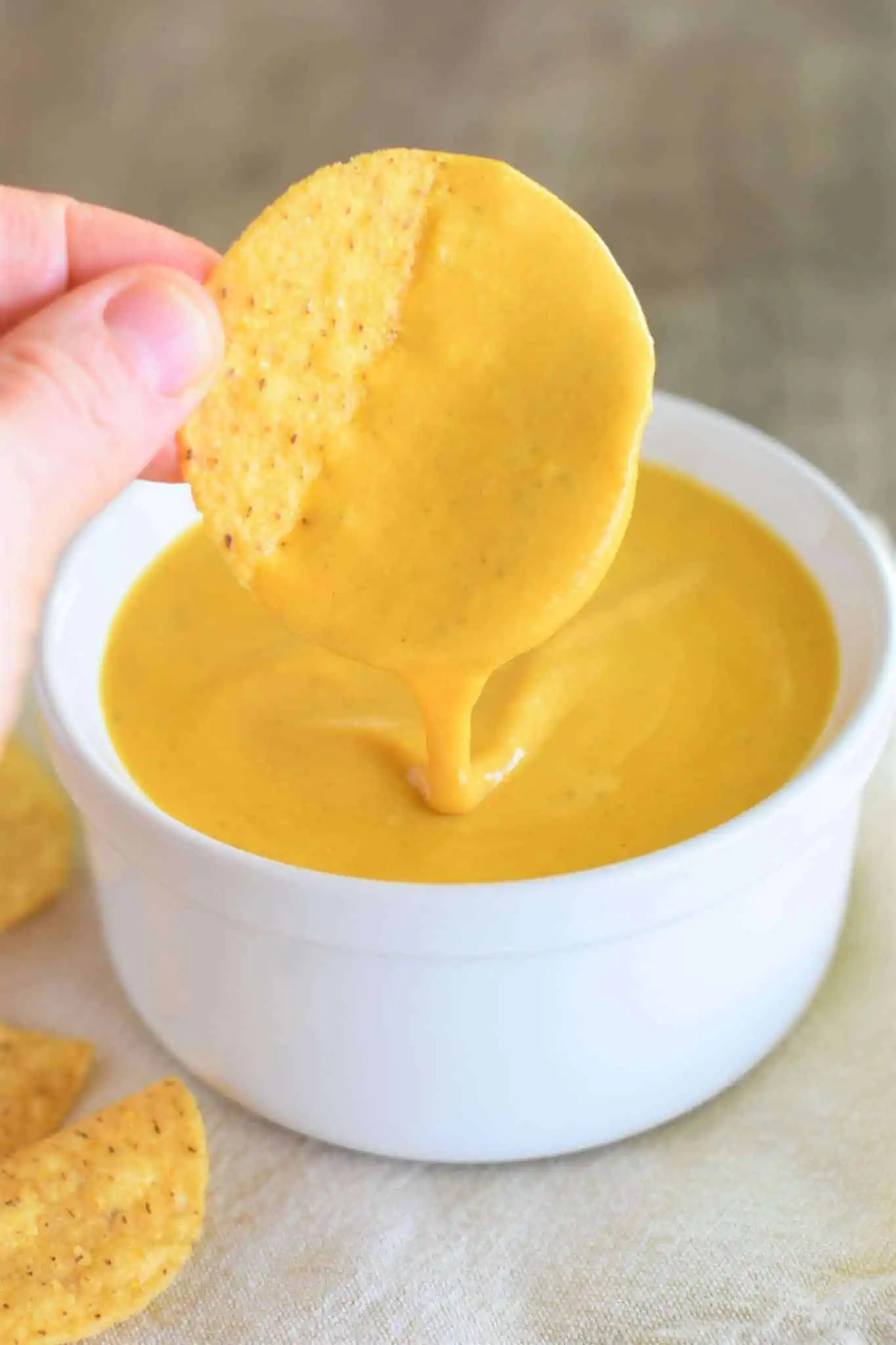 round tortilla chip being dipped into a bowl of vegan cheddar cheese sauce