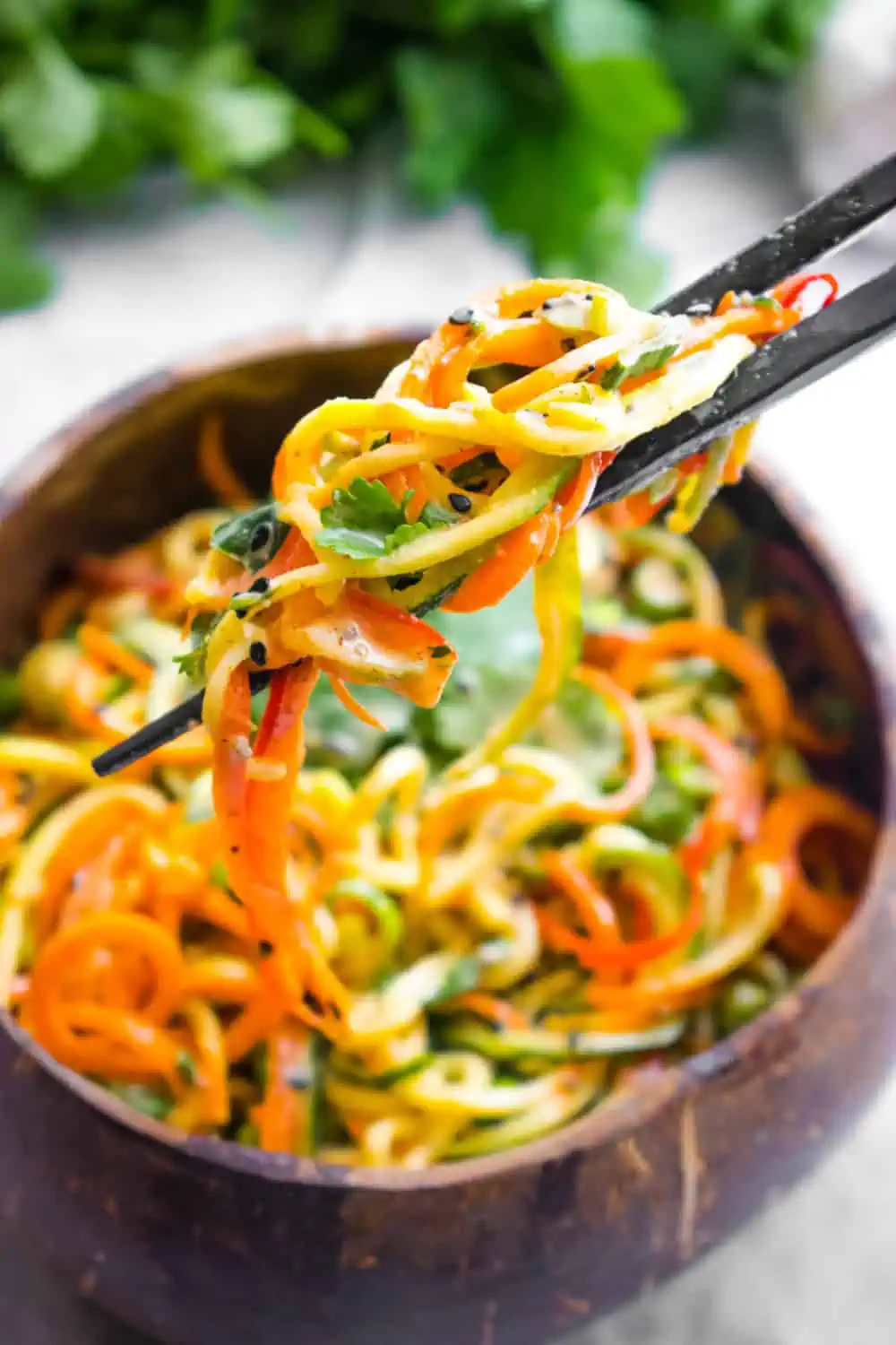 Chopsticks holding up zucchini noodles from a bowl of Asian zucchini noodles.