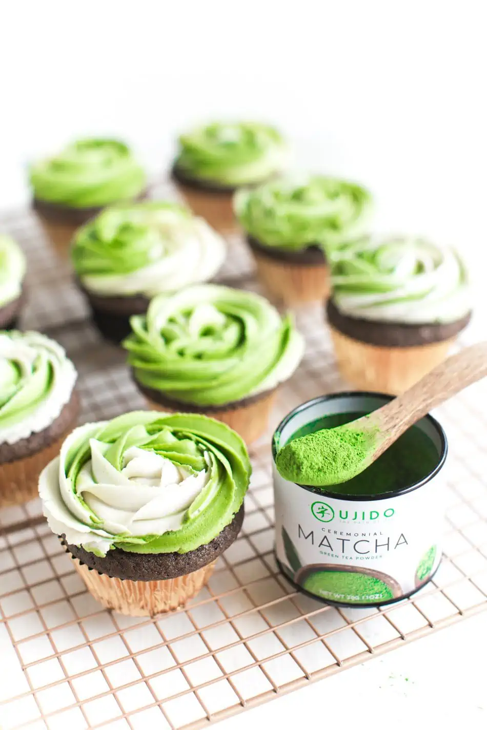 Chocolate cupcakes on a cooling rack topped with green frosting, next to a container of matcha.