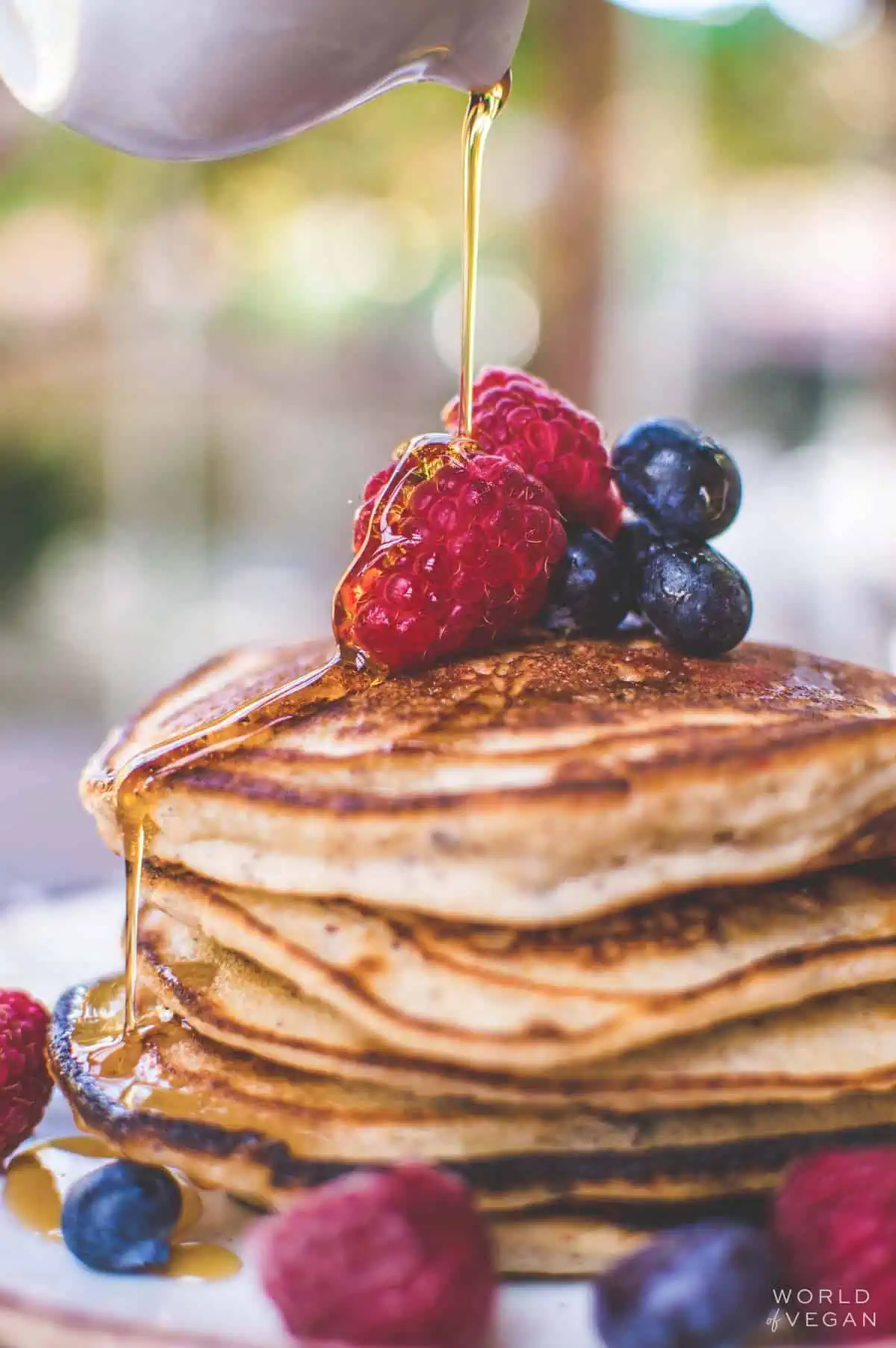 Fluffy vegan pancakes stacked on a plate with berries and maple syrup.