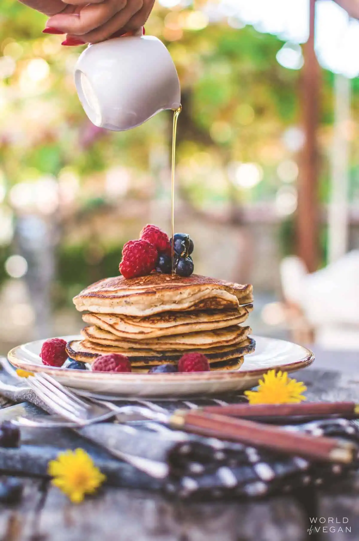 Stack of vegan pancakes on a plate, with maple syrup being poured over the top.