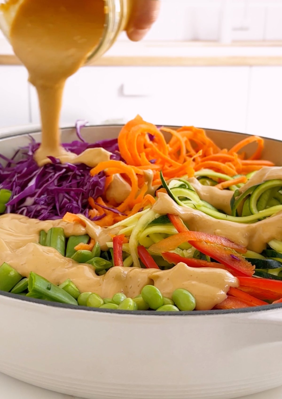 https://www.worldofvegan.com/wp-content/uploads/2019/02/pouring-peanut-dressing-on-zoodles.jpg