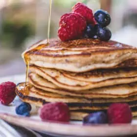 A stack of vegan pancakes on a plate with berries and drizzled with maple syrup.