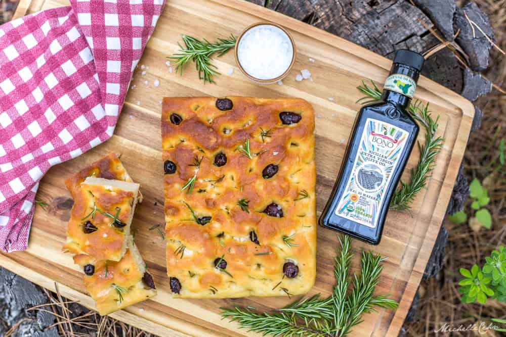 delicious picnic style focaccia bread on a wood cutting board with chunky salt olive oil and rosemary
