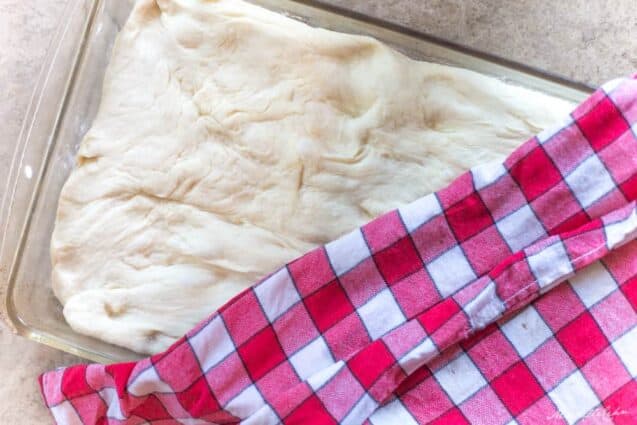 focaccia bread dough rising with checkered cloth on top