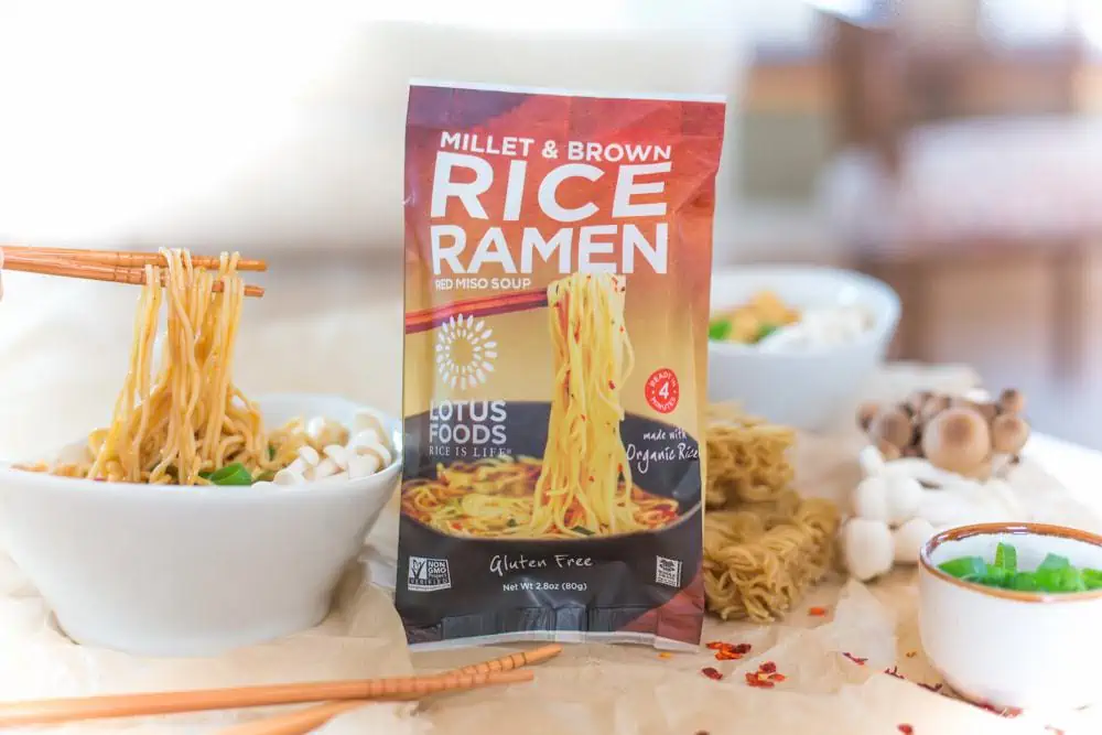 package of rice ramen noodles from Lotus Foods next to vegan ramen in a bowl being lifted up with chopsticks