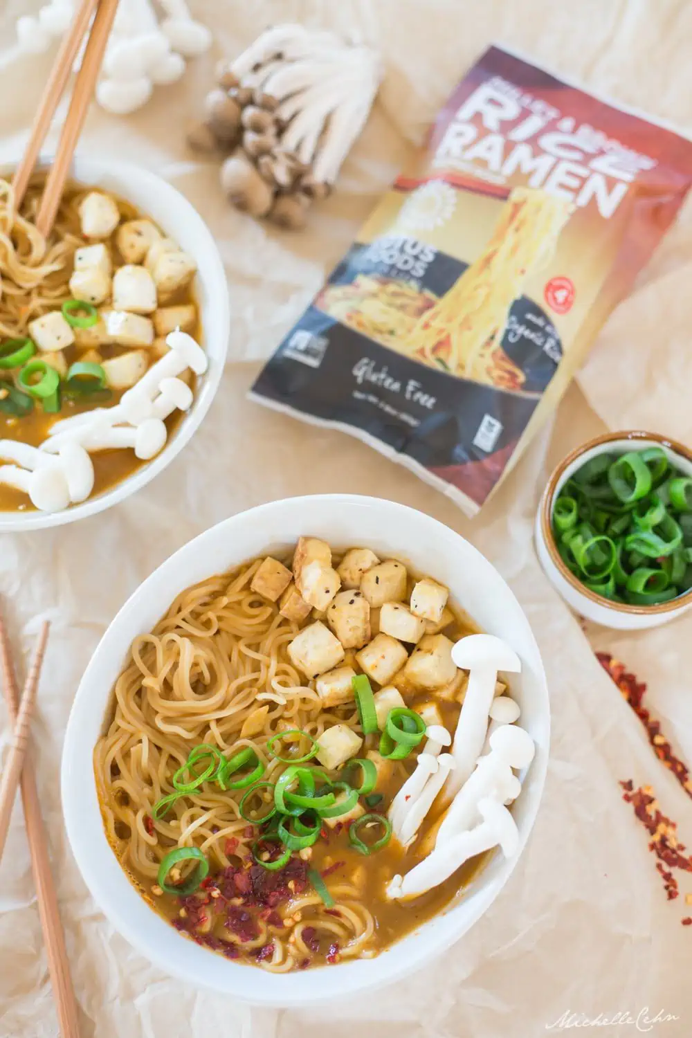 A bowl of Vegan Ramen Noodle Soup next to a Lotus Foods package of ramen and a bowl of sliced green onion. 