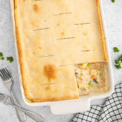 Vegan chicken pot pie in a casserole dish with a slice of the crust missing, revealing the vegetable filling.